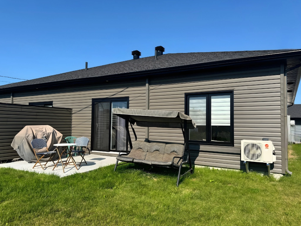 Cour arrière privée de La Place Haziel — terrasse béton, pelouse verte, thermopompe et mobilier extérieur